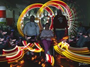 Tres participantes del CAI ASPAYM fotografiados con dibujos de luz de colores al fondo